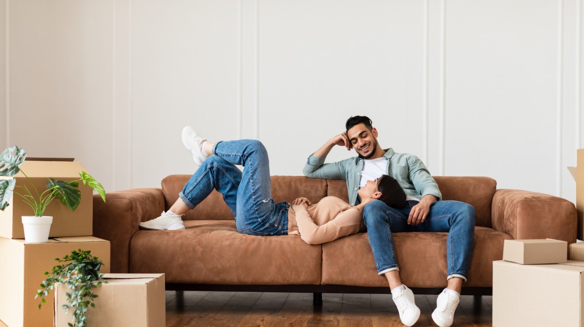 Frau und Mann auf einer Couch, die sich neben Umzugskartons anlächeln
