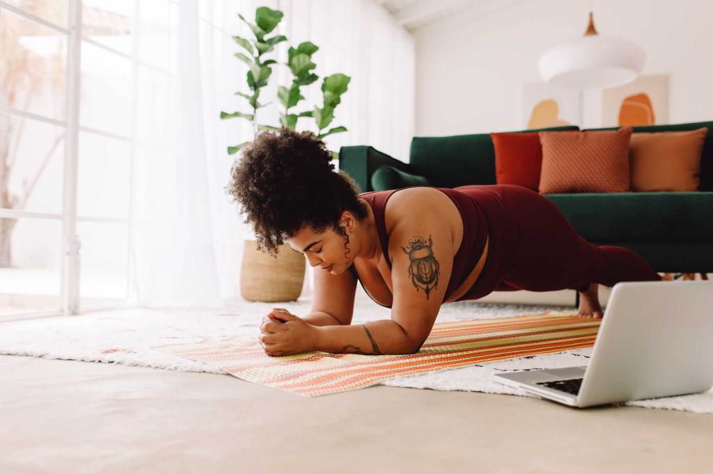 Frau macht Plank-Workout mit Laptop zu Hause