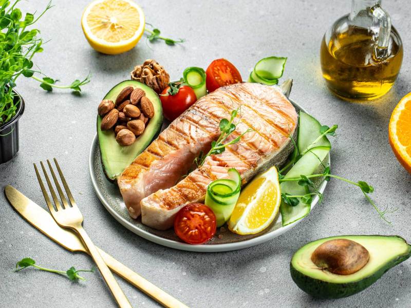 Gegrilltes Lachs-Fischsteak, Avocado, Mandeln, Öl und frischer Gemüsesalat. Ketogene Diät. Kohlenhydratarmes und fettreiches Gericht. Gesunde Ernährung Konzept.