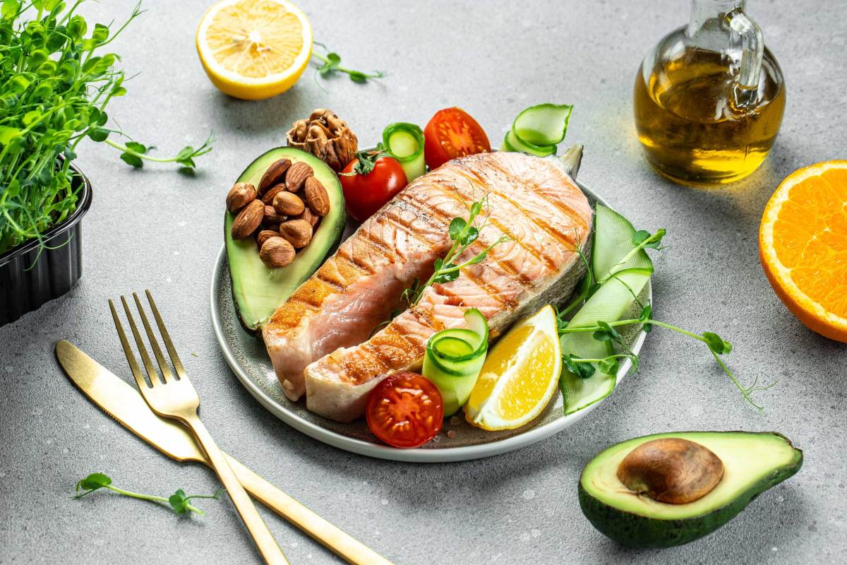 Gegrilltes Lachs-Fischsteak, Avocado, Mandeln, Öl und frischer Gemüsesalat. Ketogene Diät. Kohlenhydratarmes und fettreiches Gericht. Gesunde Ernährung Konzept.