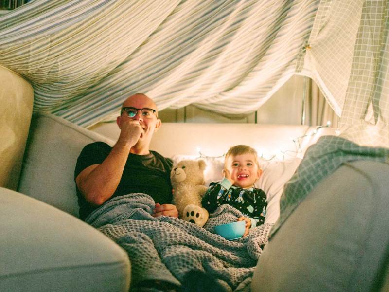 Vater und Sohn in einer selbstgebauten Höhle schauen einen Film und essen Popcorn.