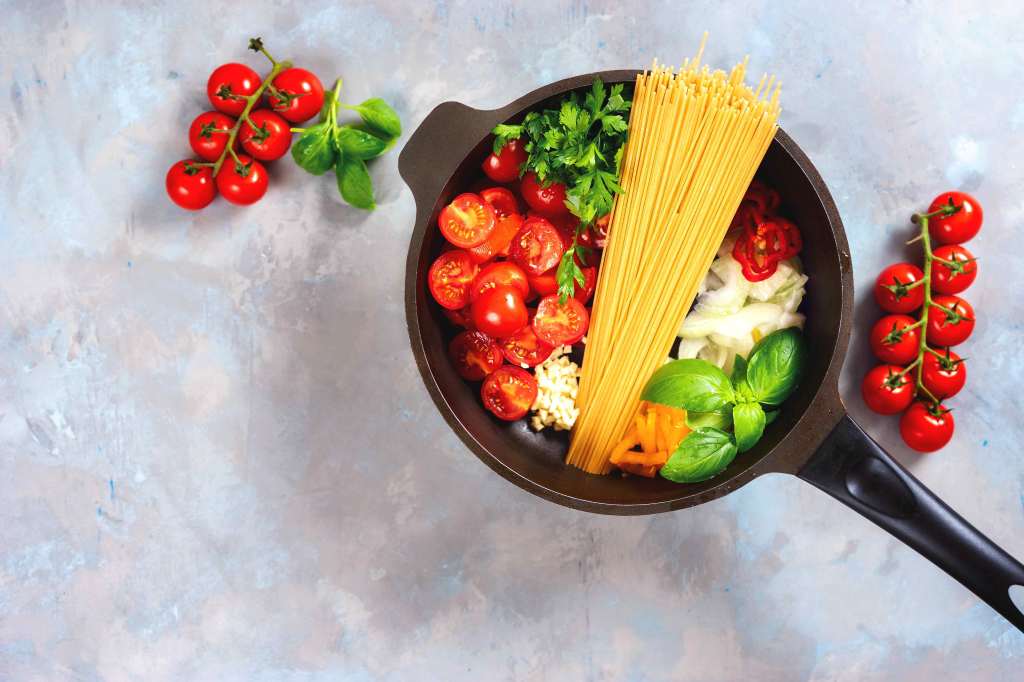 Topf von oben gefüllt mit Spaghetti, halbierten Kirschtomaten, Zwiebeln und Kräutern.