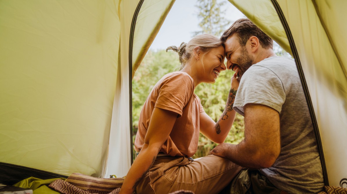Frau und Mann in einem Zelt in der Natur, die sich anlächeln und sich mit der Stirn berühren