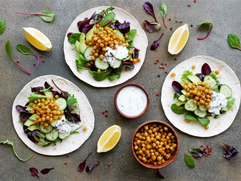 Veganer Tortilla-Kichererbsen-Avocado-Salat mit Gurke und Joghurtsoße. Gesundes Clean Eating Food Konzept. Gesundes Essen, angerichtet auf weißen Tellern.