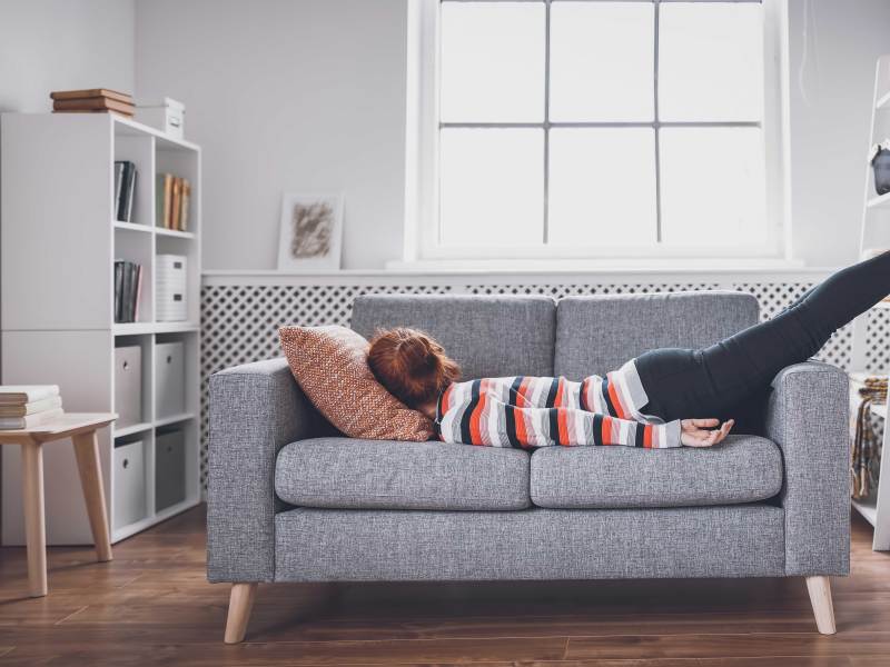 Frau lässt sich geschafft aufs Sofa fallen.