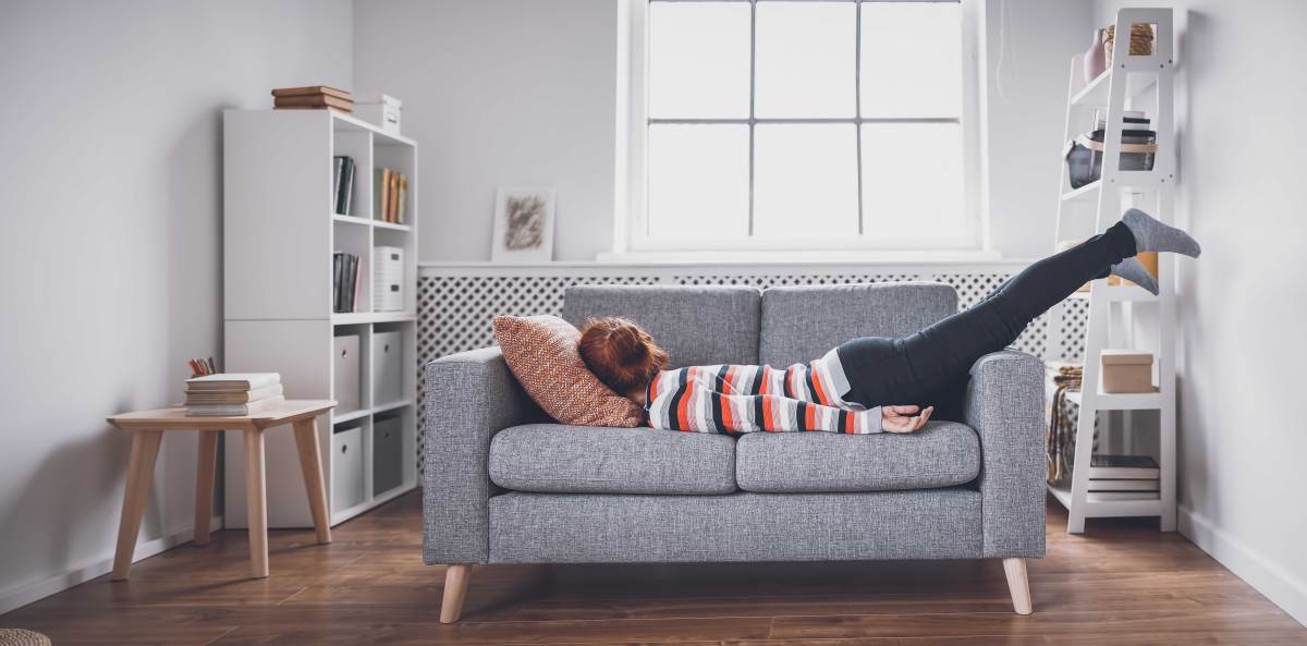 Frau lässt sich geschafft aufs Sofa fallen.