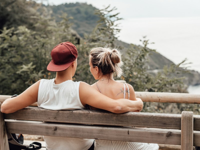 Mann und Frau sitzen im Sommer auf Parkbank und umarmen sich