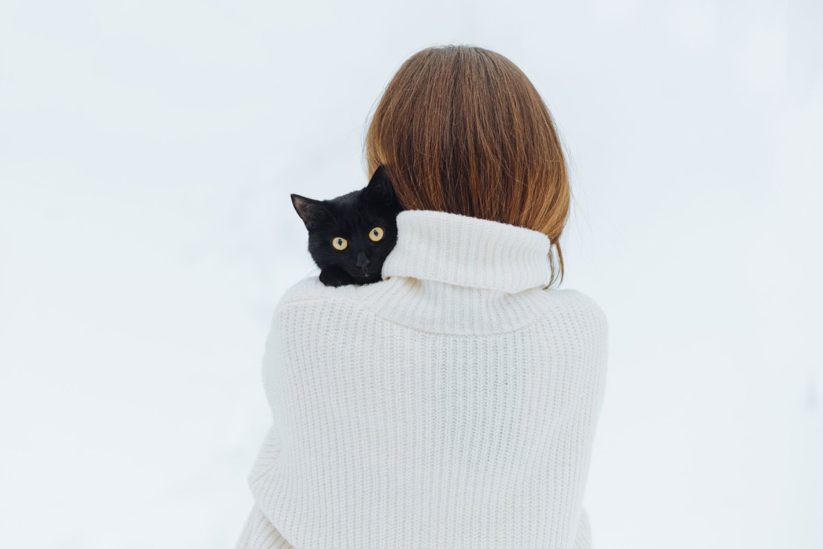 Frau mit einem weißen Pullover und einer schwarzen Katze auf dem Arm