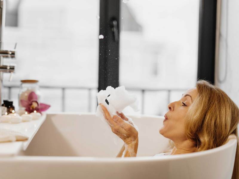 Nahaufnahme einer Frau, die zu Hause in der Badewanne Schaum aus der Hand pustet.