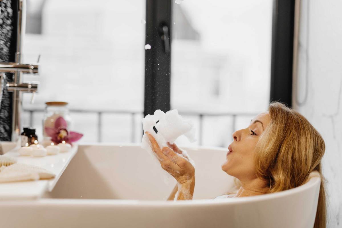 Nahaufnahme einer Frau, die zu Hause in der Badewanne Schaum aus der Hand pustet.