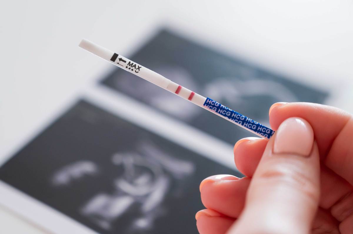 Nahaufnahme eines positiven Schwangerschaftstests vor einem Ultraschallbild.
