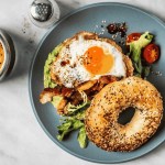 Bagel-Sandwich mit Avocado, Spiegelei und Beilagensalat und Kaffee auf weißem Hintergrund
