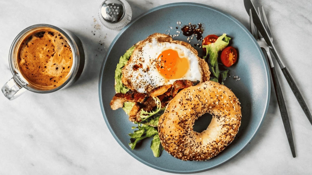 Bagel-Sandwich mit Avocado, Spiegelei und Beilagensalat und Kaffee auf weißem Hintergrund