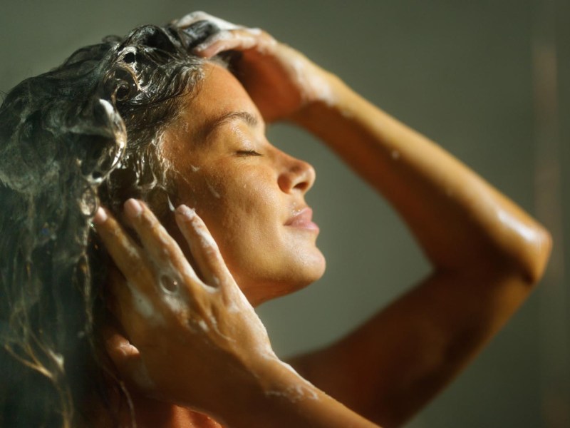 Junge Frau steht unter der Dusche und schäumt sich die Haare