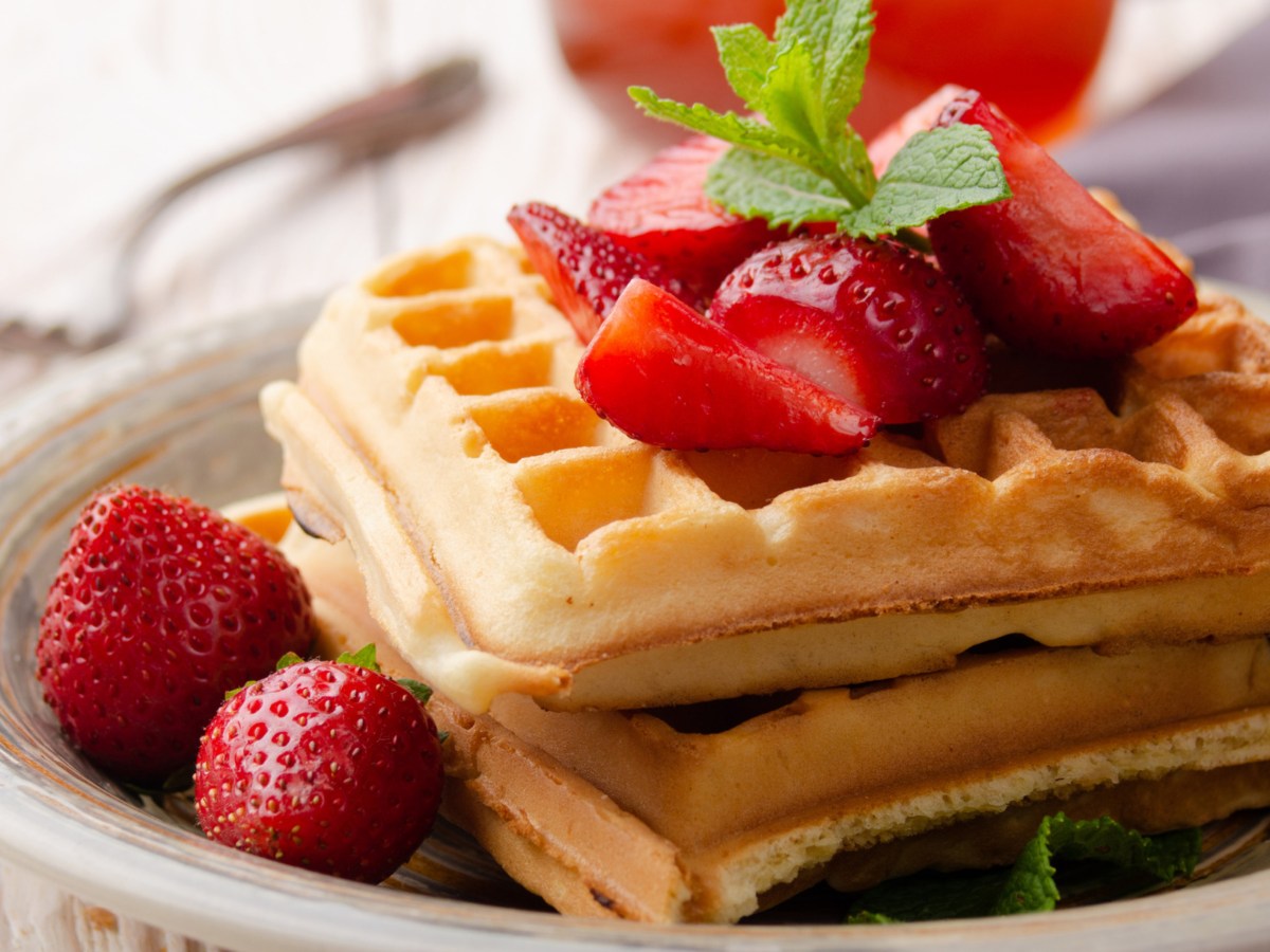 Waffeln auf einem weißen Teller, dazu frische Erdbeeren.
