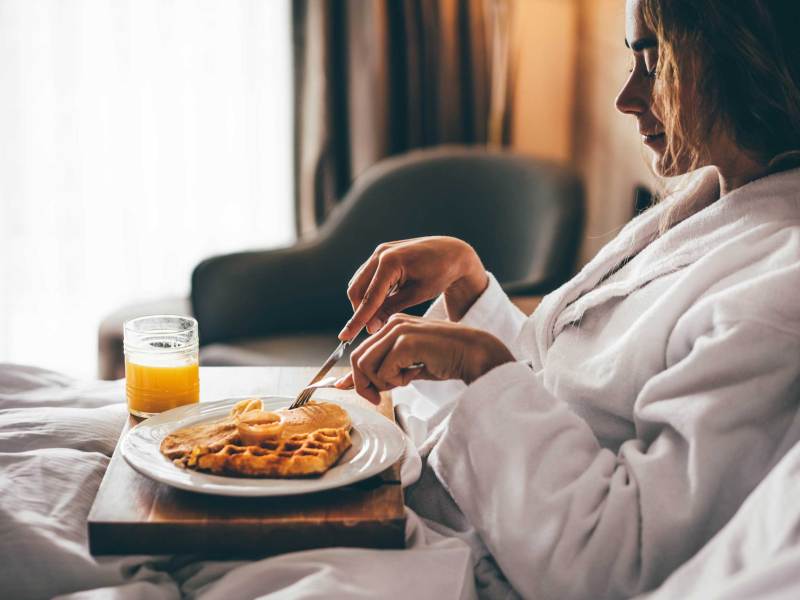 Frau beim Frühstück im Hotelzimmer. Waffeln zum Frühstück