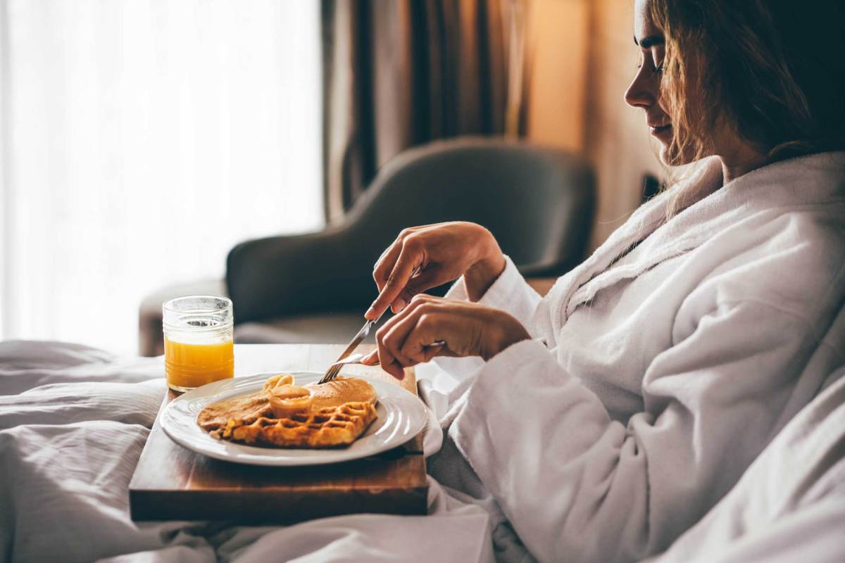 Frau beim Frühstück im Hotelzimmer. Waffeln zum Frühstück