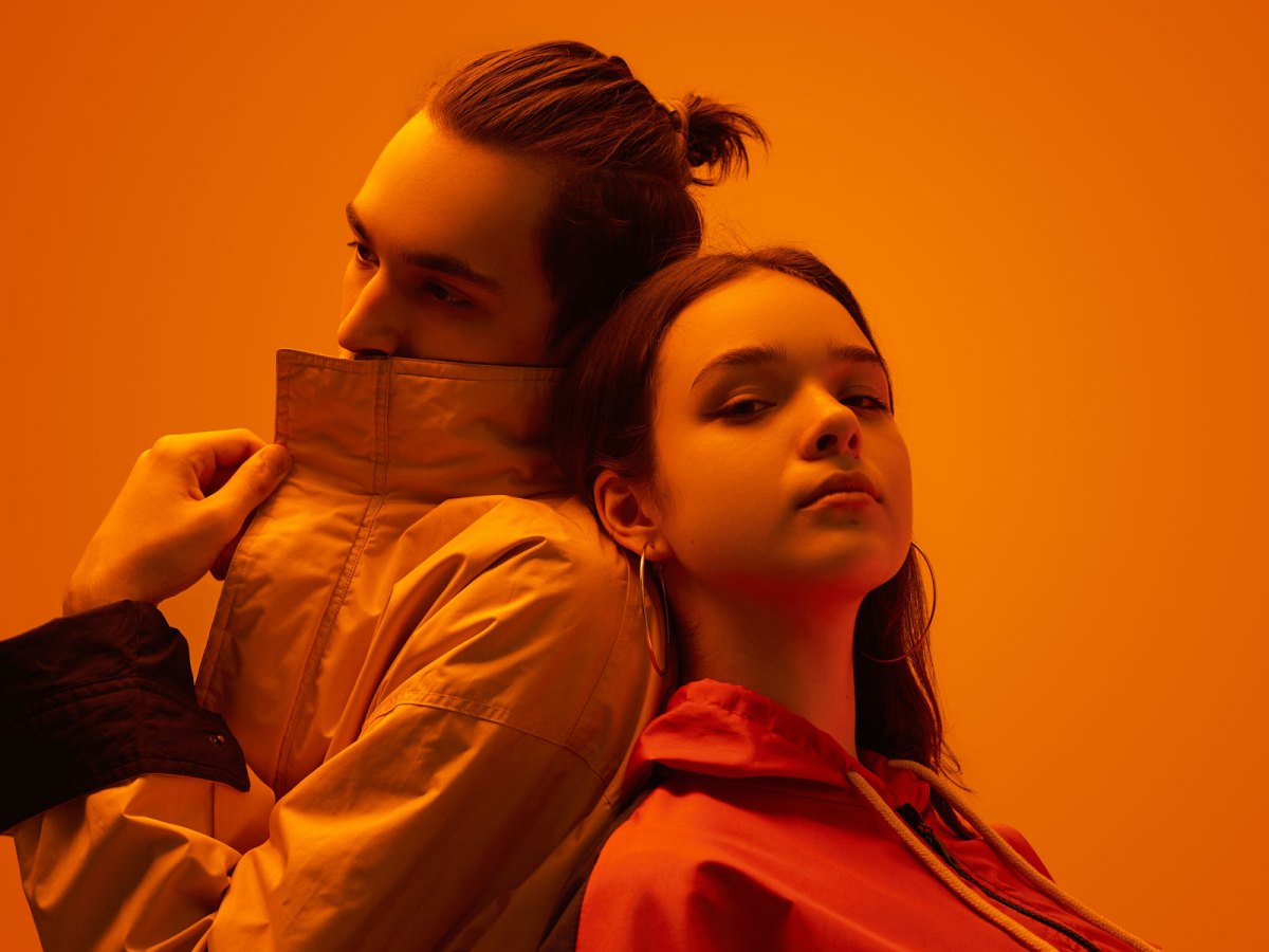 Junges Paar vor einer orangen Wand in orangem Licht