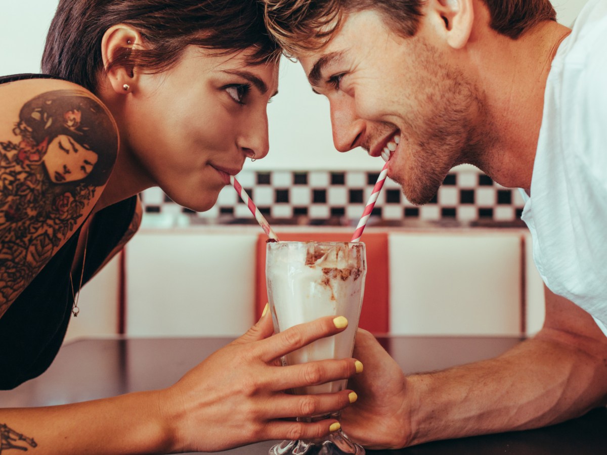 Eine Frau und ein Mann sind auf einem Date und teilen sich einen Milkshake.