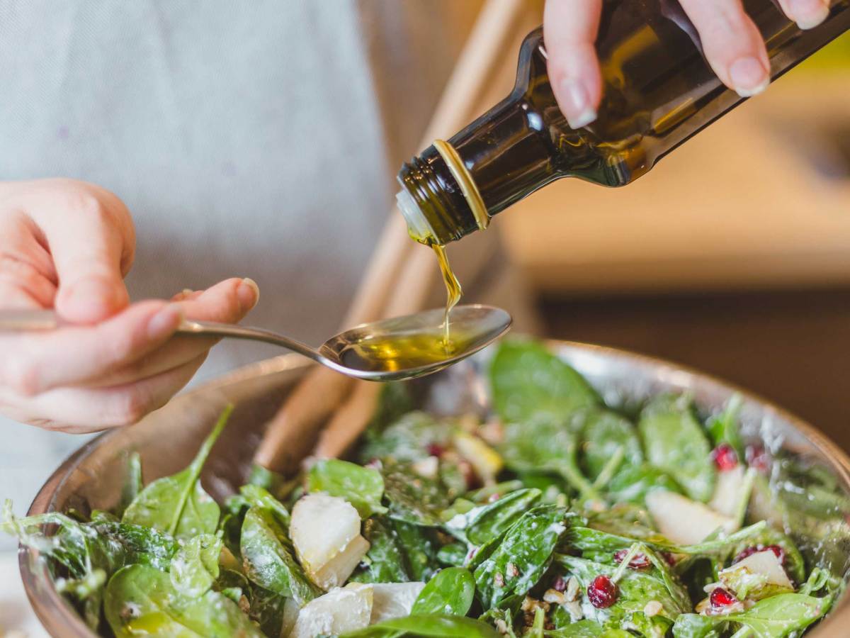 Nahaufnahme von Händen, die natives Olivenöl über Salat gießen