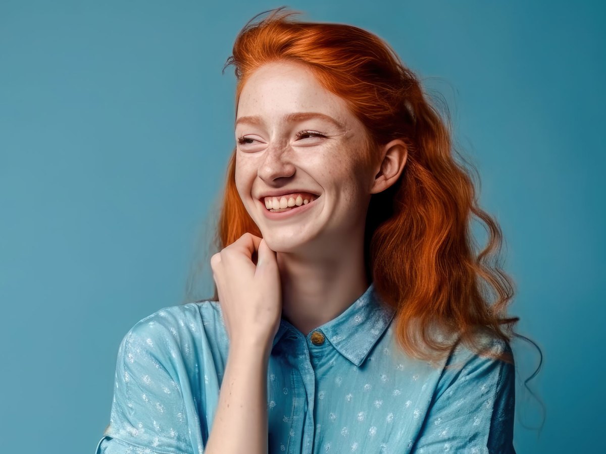 Frau mit roten Haaren steht vor einer blauen Wand und lächelt