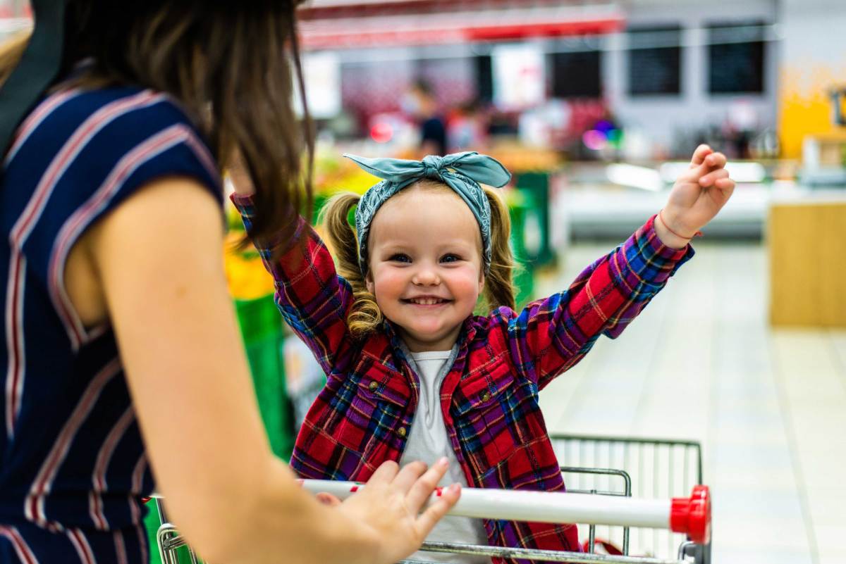 Mutter schiebt ihre Tochter im Einkaufswagen durch den Supermarkt.