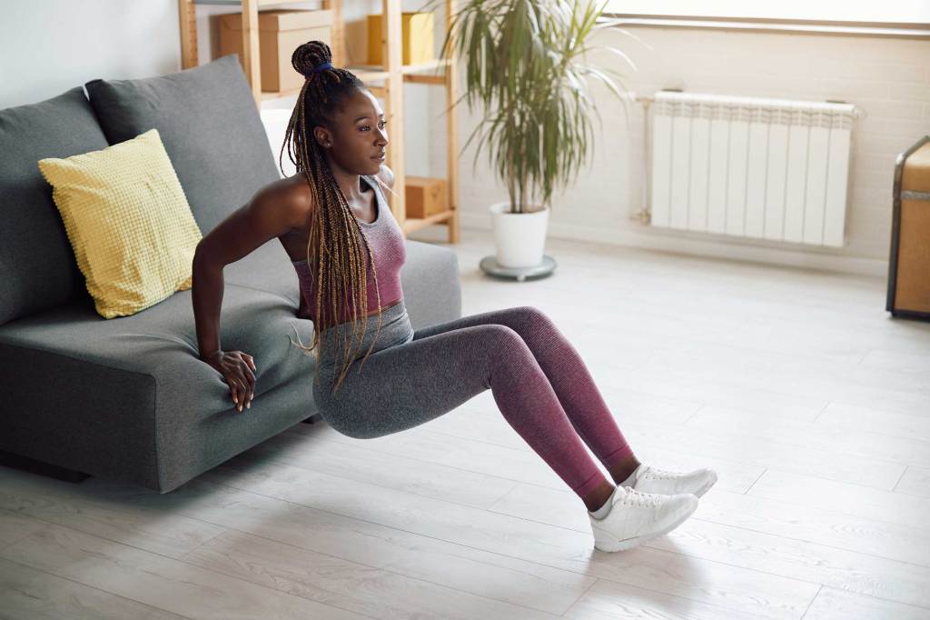 Sportliche Frau macht Trizeps-Dips, während sie sich zu Hause auf das Sofa lehnt.