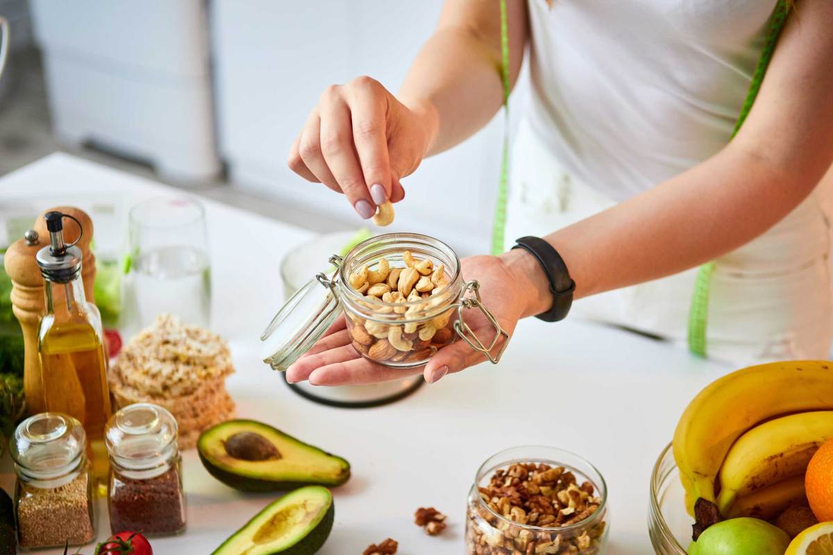 Junge glückliche Frau isst verschiedene Nüsse (Cashew, Haselnuss, Mandel) in der modernen Küche. Gesunde Ernährung und Diät-Konzept. Gewicht zu verlieren