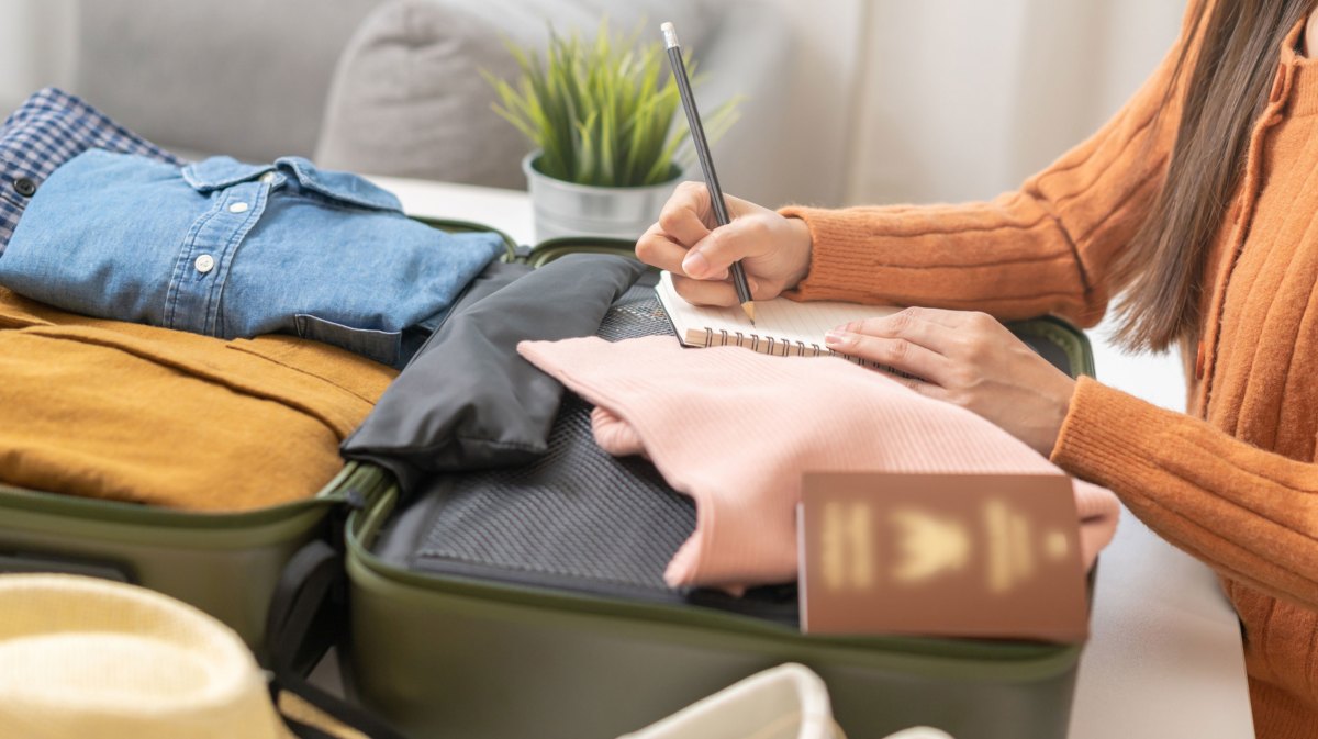 Frau erstellt Packliste für Urlaub auf gepacktem Koffer