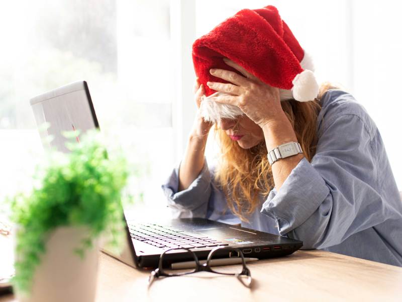 Frau mit Weihnachtsmann-Mütze sitzt verzweifelt vor ihrem Laptop und schlägt die Hände vor die Augen.