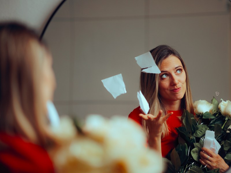Frau in einem Spiegel, die Blumen in der Hand hält und einen Zettel zerreißt