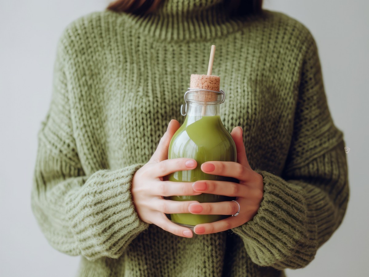 Frau mit grünem Pulli, die einen grünen Saft in einer Glasflasche mit Strohhalm in der Hand hält