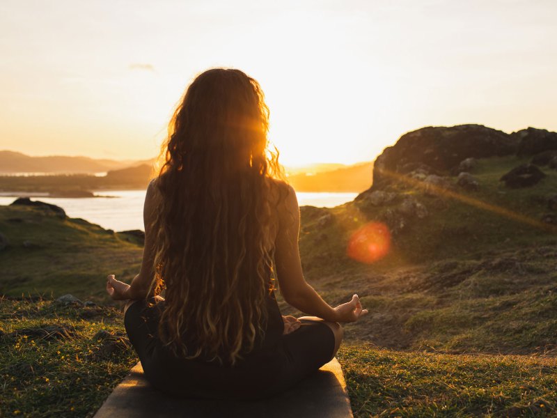 Frau sitzt im Schneidersitz im Sonnenuntergang und meditiert