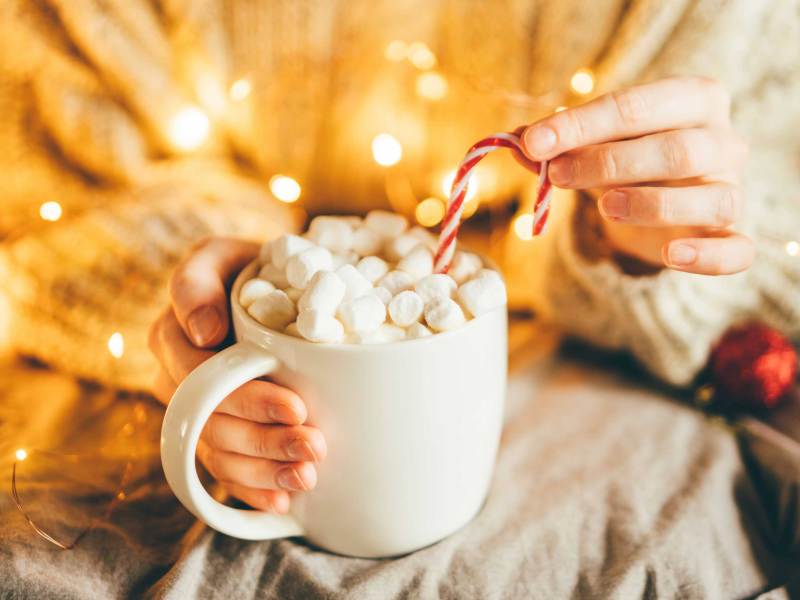 Frau hält Tasse mit heißer Schokolade, Marshmallows und Zuckerstange