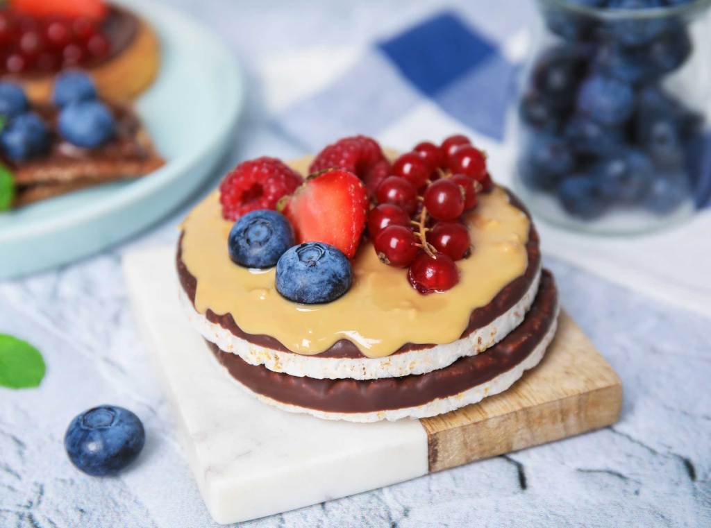 Kalorienarme Süßigkeiten Reiswaffeln mit Schokolade, Beerenfrüchten und Erdnusscreme auf hellem Untergrund