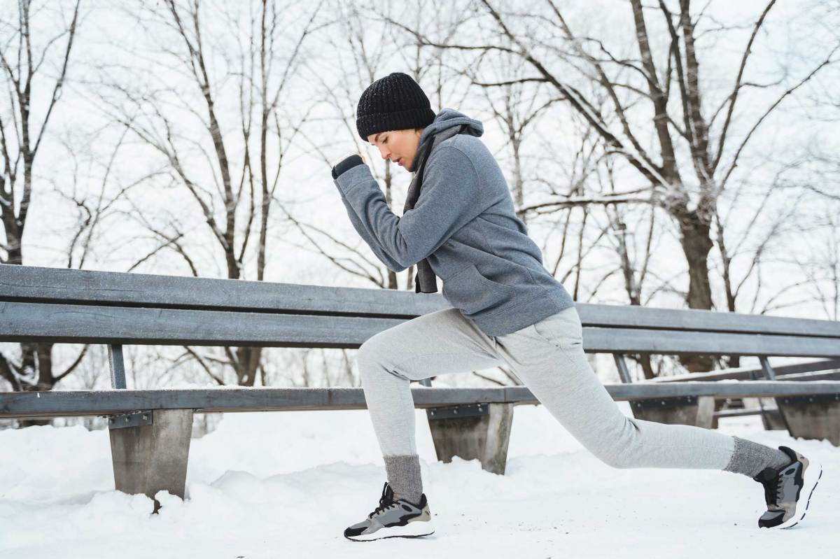 Sportliche Frau beim Aufwärmen vor ihrem Jogging-Training an einem verschneiten Wintertag in einem Stadtpark