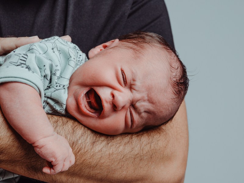 Weinendes Baby, dass auf dem Unterarm eines Mannes liegt.