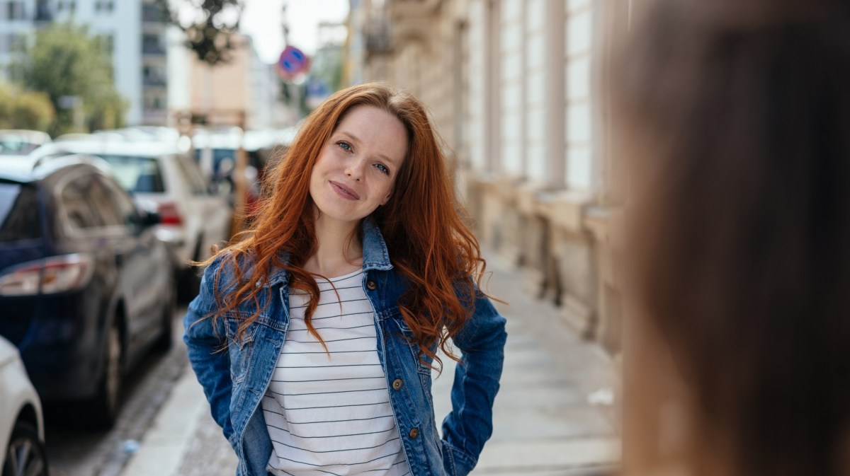 Frau mit roten Haaren auf der Straße, die einer anderen Frau mit langen braunen Haaren zuhört und anschaut