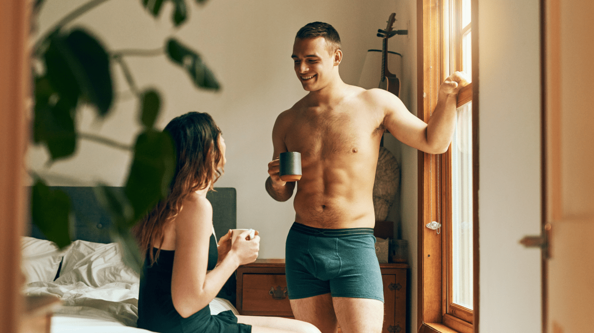Mann und Frau im Schlafzimmer, die Kaffeetrinken, sich unterhalten und anlachen.
