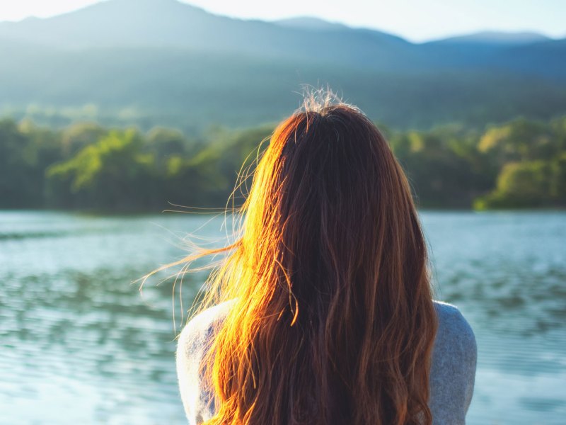 Eine junge Frau sitzt an einem See und schaut auf das Wasser