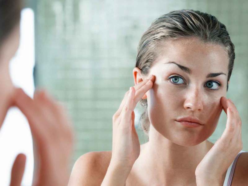 Frau cremt sich vor dem Spiegel das Gesicht mit Feuchtigkeitscreme ein.