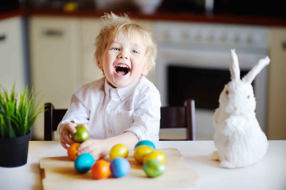 Kleiner Junge am Küchentisch freut sich über die bunten Ostereier.