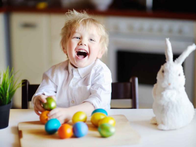 Kleiner Junge am Küchentisch freut sich über die bunten Ostereier.