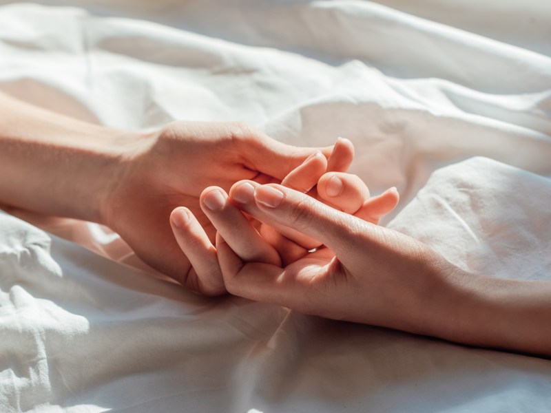 Zwei Hände auf einer Bettdecke, die sich gegenseitig halten