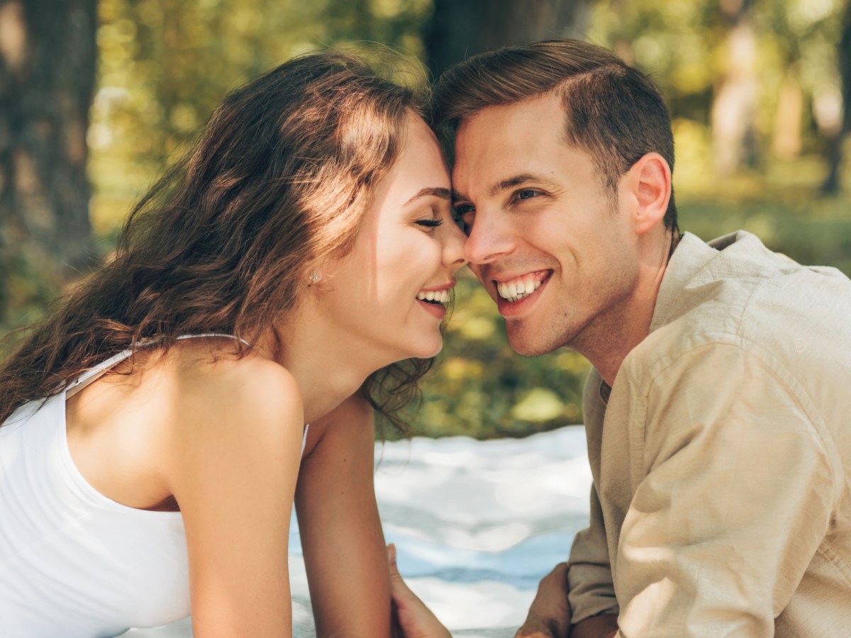 Frau und Mann im Park auf einer Decke im Sommer, die sich anlächeln