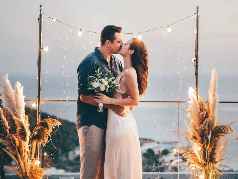 Frau und Mann küssen sich vor einer Strandkulisse und einer Lichterkette mit ganz viel Deko.