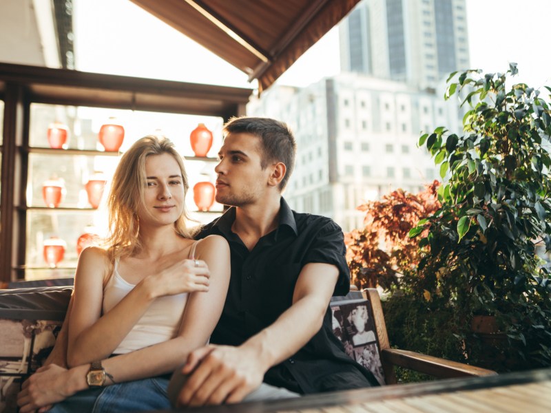 Mann und Frau in Café, die in der Sonne draußen sitzen und sich umarmen