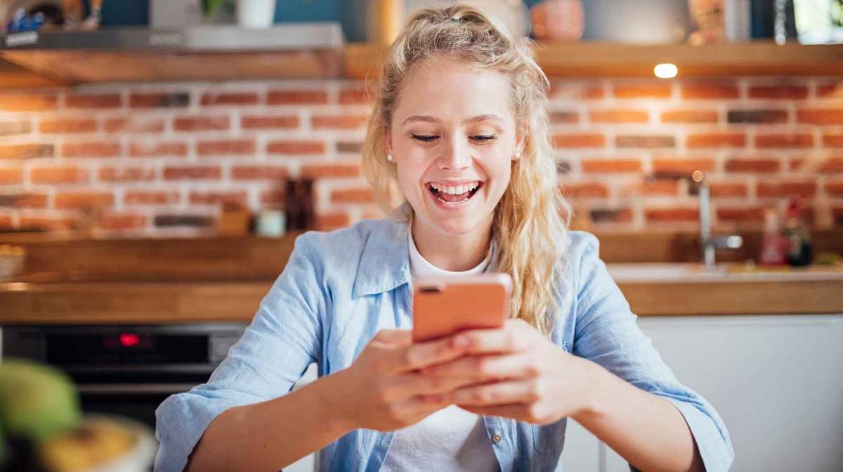 Junge blonde Frau sitzt an ihrem Handy.
