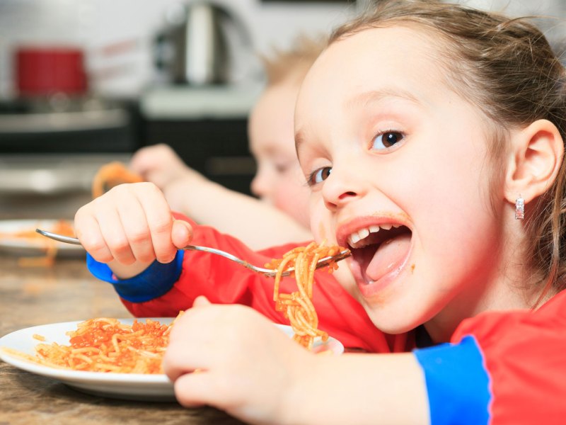 Mädchen, ca. 6 Jahre alt, isst eine Portion Spaghetti mit Tomatensauce am Küchentisch.