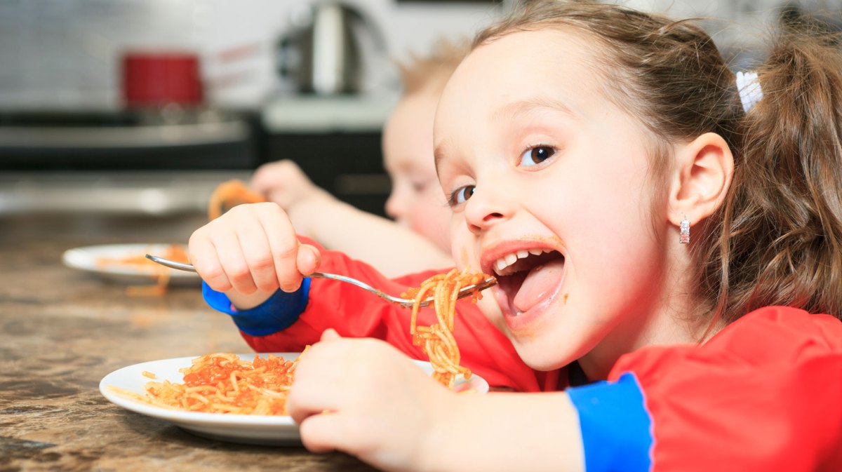 Mädchen, ca. 6 Jahre alt, isst eine Portion Spaghetti mit Tomatensauce am Küchentisch.